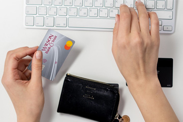 A person holding a credit card with their left hand and typing on a keyboard with their right hand. 
